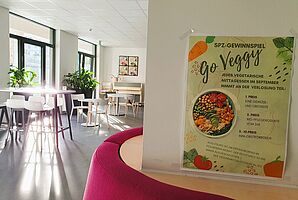 Blick in den Speisesaal der Übergangseinrichtung mit einem Plakat im Vordergrund, das eine Nudging-Aktion für vegetarisches Essen bewirbt.