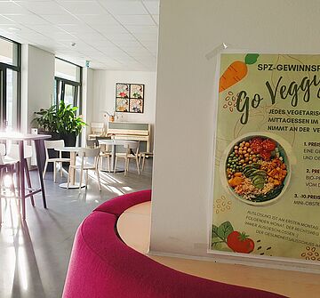 Blick in den Speisesaal der Übergangseinrichtung mit einem Plakat im Vordergrund, das eine Nudging-Aktion für vegetarisches Essen bewirbt.